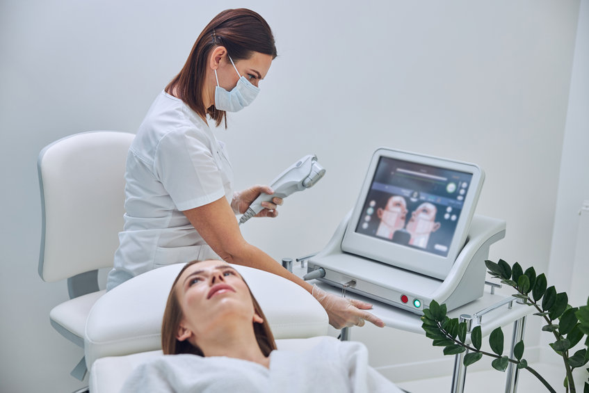 Waist up portrait of focused beautician standing near the modern ultrasound device and integrating he program for the skin treatment in spa salon